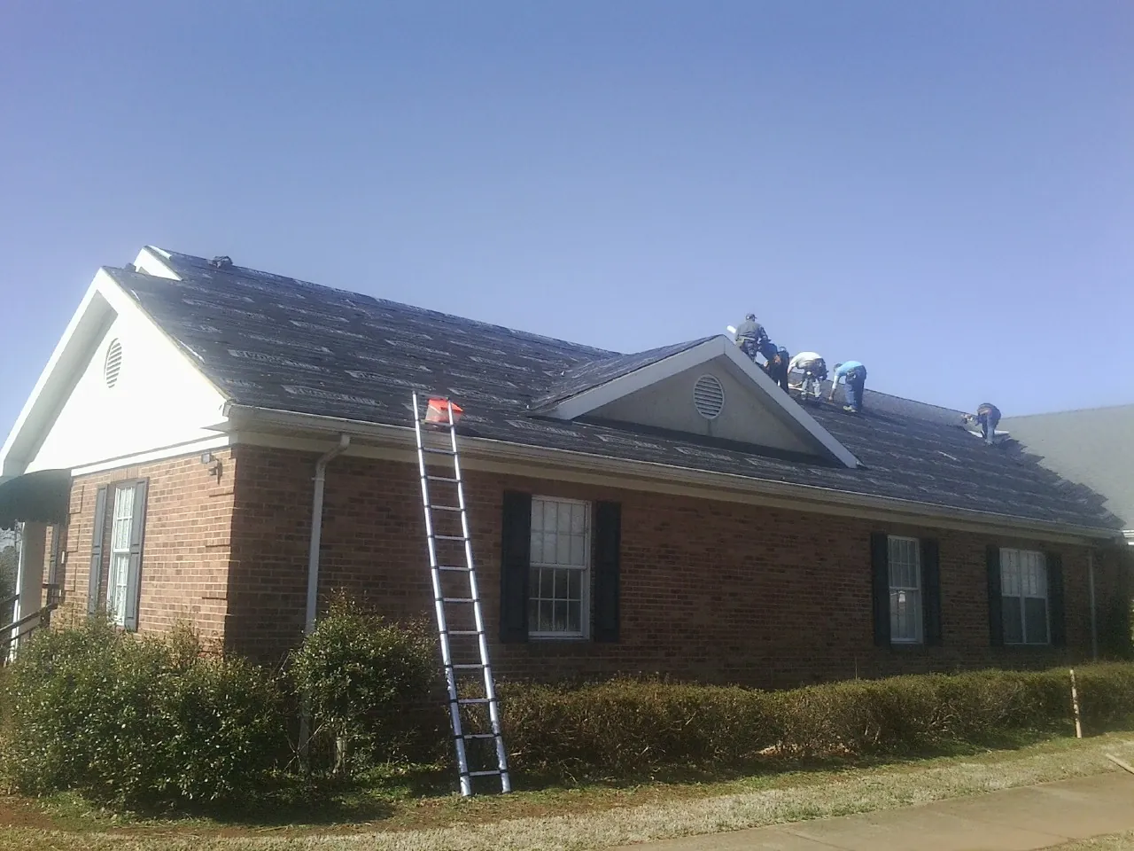 Crew tearing shingles off a brick ranch roof with a ladder set — Emergency Roof Repair work by our crew in Ventura