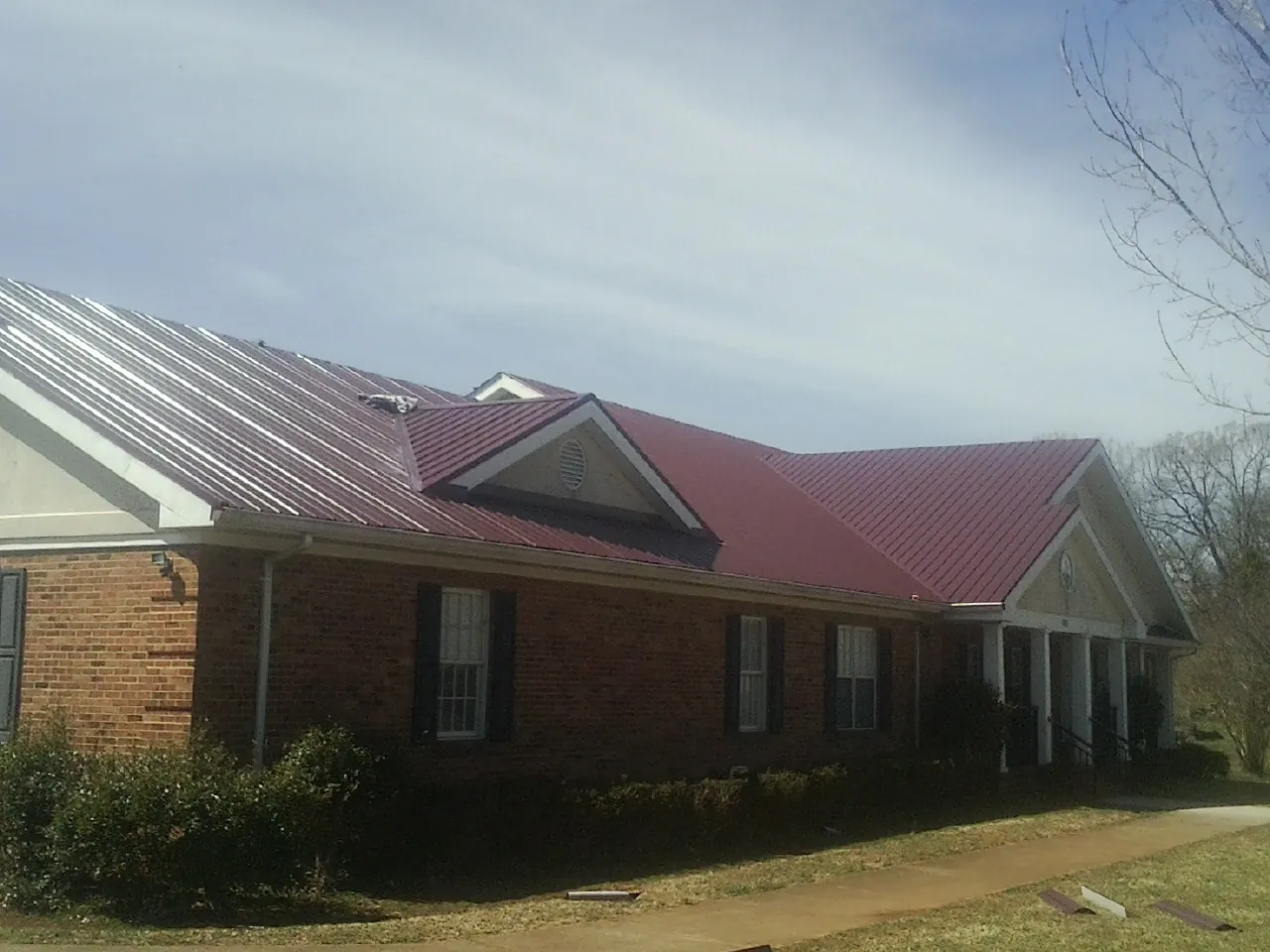 Red metal roof with gabled entries on a long brick building, from a Hail Damage Roof Repair job in Ventura